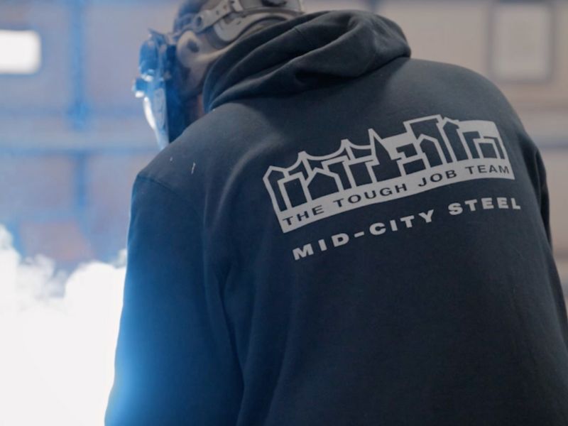 mid-city-steel-about-certification-branded-hoodie-on-welder-sparks-mask-800x600