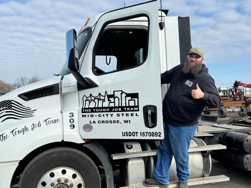 Bearded man in a cap gives a thumbs up, standing beside a white truck labeled Mid-City Steel, La Crosse, WI.