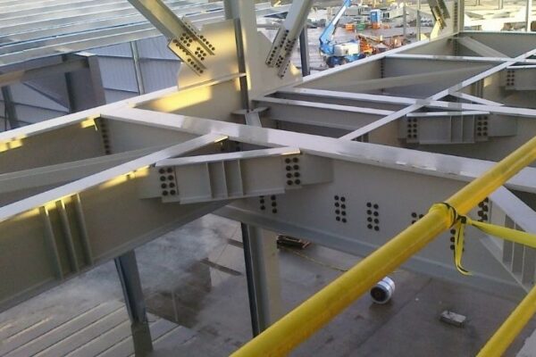 mid-city-ORC-insitutional-project-gallery-2 Steel beams and joints forming part of a building structure, viewed from above with yellow safety railing in front.
