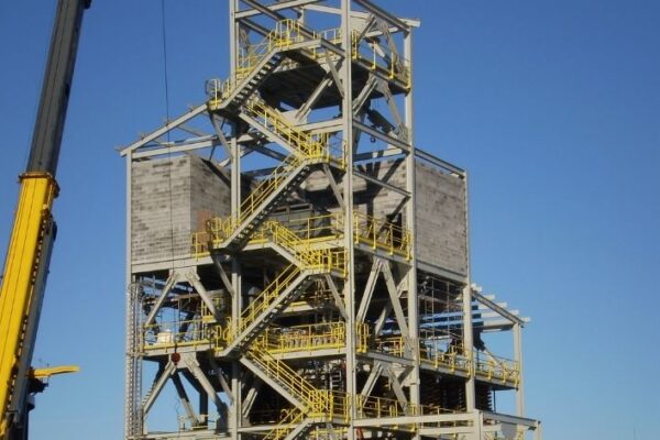 mid-city-ORC-insitutional-project-gallery-3 A multilevel steel industrial structure with yellow railings and stairs, under construction, against a clear blue sky.