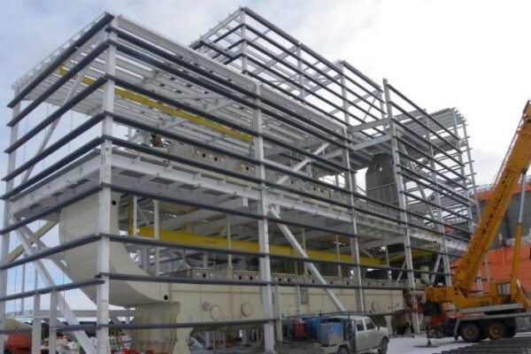 Steel framework of a multi-story building under construction with cranes and vehicles on site.