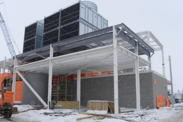 A large industrial building under construction with steel beams, concrete blocks, and snow on the ground.