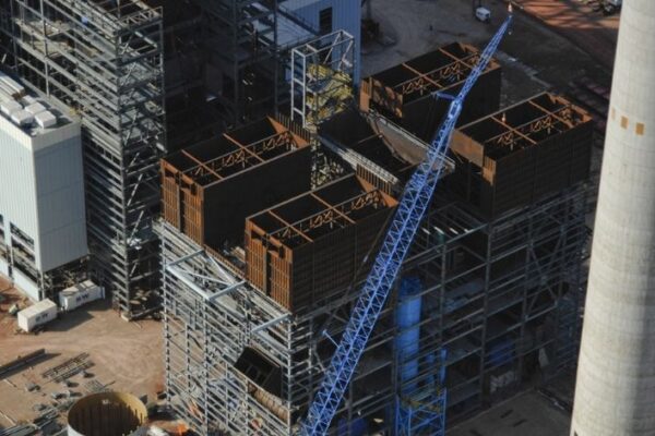Aerial view of a construction site with steel frameworks, a blue crane, and part of a smokestack visible.