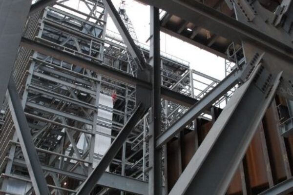 View from below of a complex steel structure, showing beams, girders, and scaffolding at a construction site.