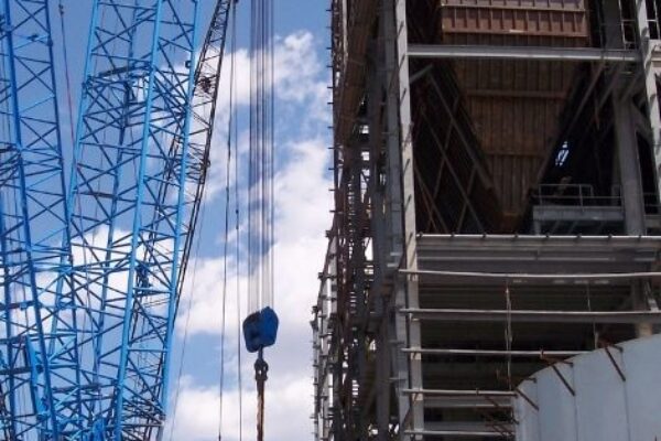 A blue crane lifts materials beside a partially constructed industrial building on a sunny day.