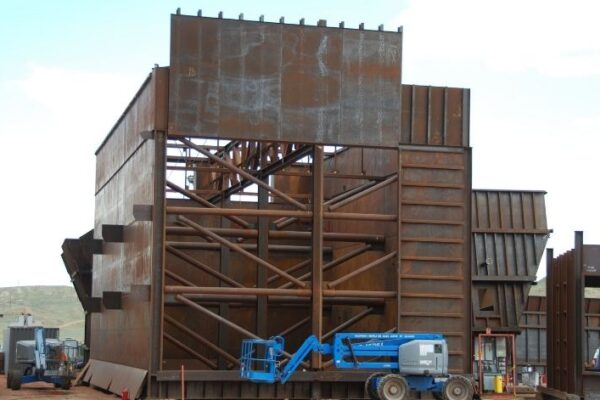 Large, rust-colored industrial steel structure with scaffolding and a blue lift parked in front.