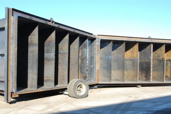 Two large, empty industrial metal containers with open sides and a single loose tire on the ground between them.