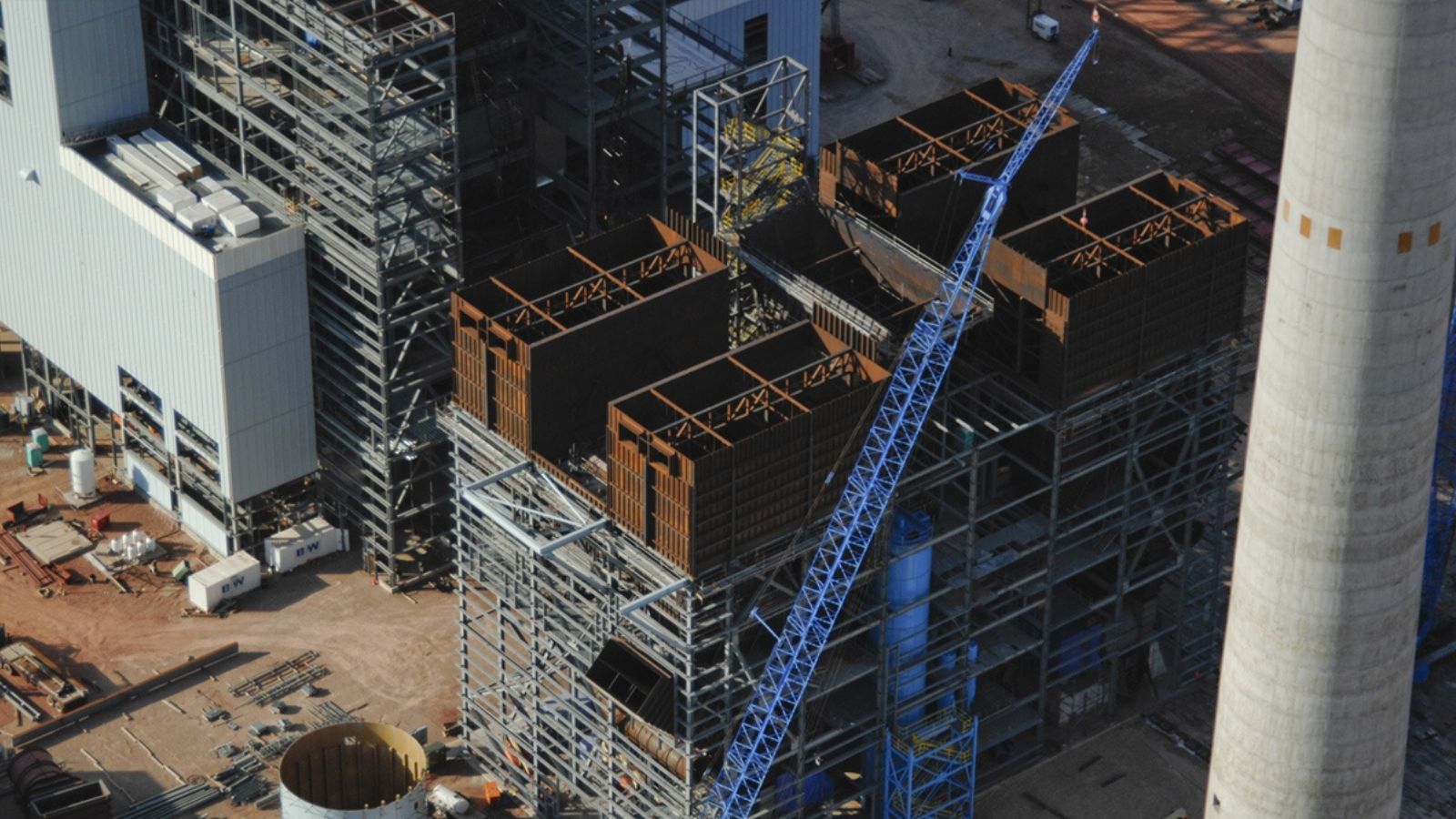 Aerial view of an industrial construction site with steel frameworks, a blue crane, and surrounding equipment.