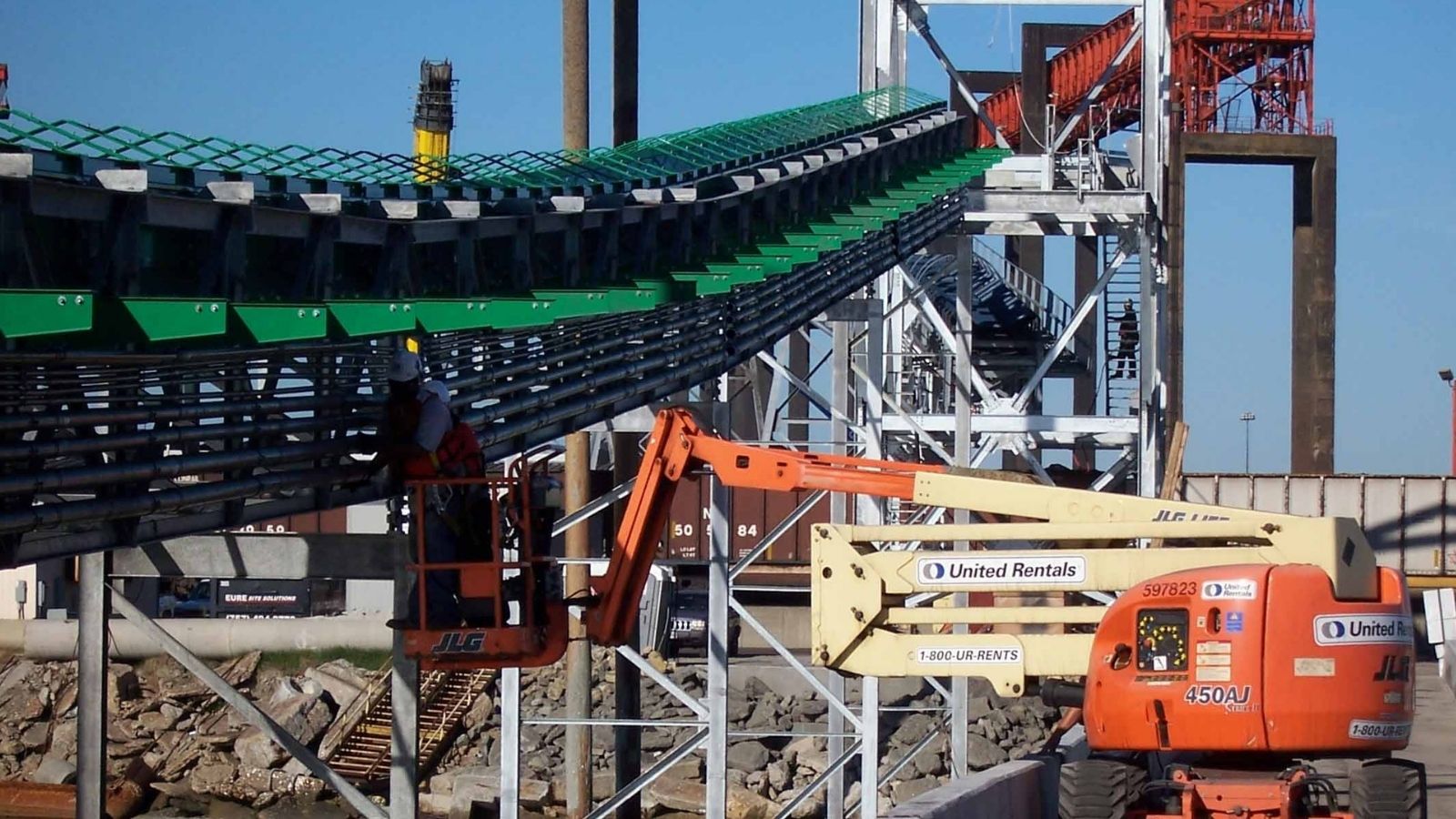 Construction workers on elevated lifts working on a large industrial conveyor system with metal structures and machinery.
