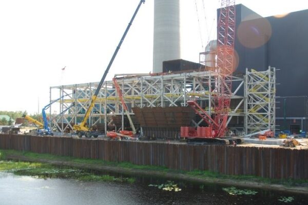 Construction site with cranes and scaffolding beside a building and pond, under a partly cloudy sky.