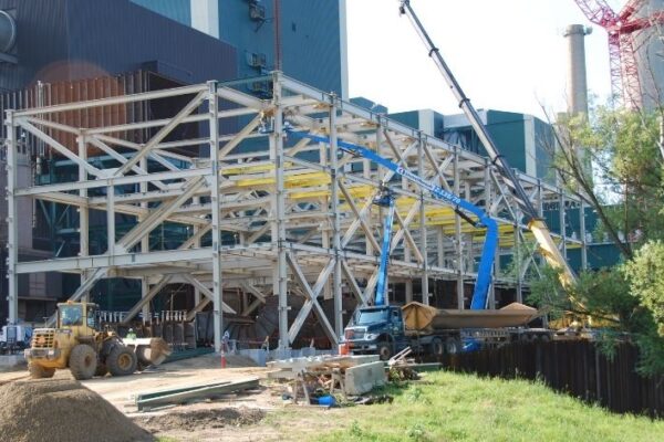 Steel-frame building under construction with cranes, trucks, and construction equipment at work on site.