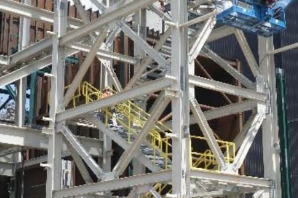 A construction site with steel framework, a blue lift elevated, and an orange lift parked on the ground.