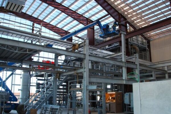 mid-city-steel-cow-canyon-central-processing-facility-industrial-gallery-2 Interior of an industrial building under construction with metal beams, scaffolding, and workers on elevated platforms.