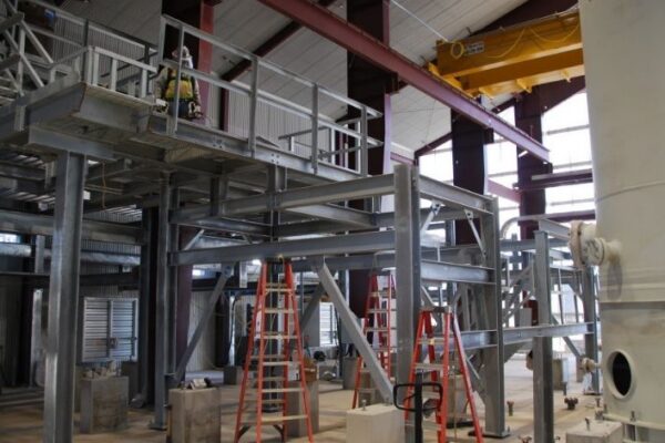 mid-city-steel-cow-canyon-central-processing-facility-industrial-gallery-5 Industrial facility under construction with metal platforms, red ladders, and overhead crane inside a large building.