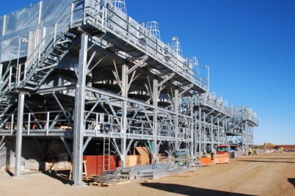 mid-city-steel-cow-canyon-central-processing-facility-industrial-gallery-6 Large industrial metal structures with stairs and walkways at a construction site under a clear blue sky.