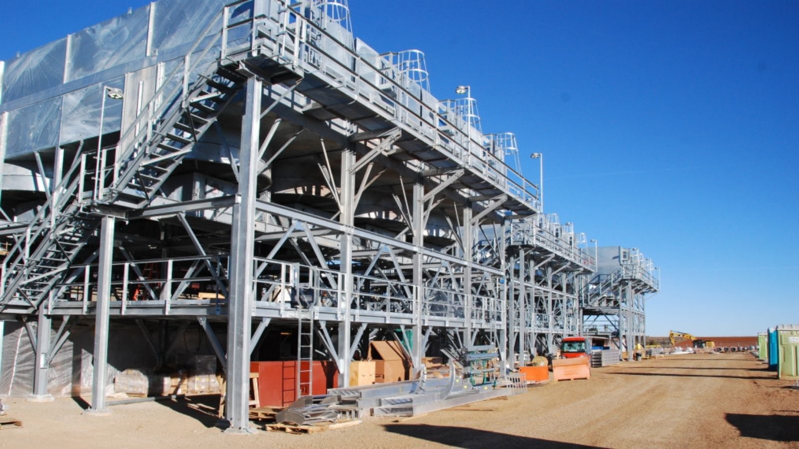 Large industrial metal structure with stairs and platforms at a construction site under a clear blue sky.