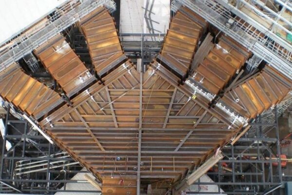 Aerial view of an industrial steel structure under construction with rust-colored metal panels and scaffolding.