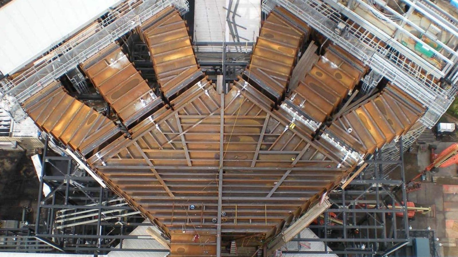 Aerial view of a large, rusted steel V-shaped industrial structure with walkways and scaffolding.