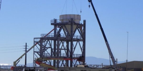mid-city-steel-drake-cement-industrial-gallery-7 A crane lifts a large cylindrical structure onto a metal framework at an industrial construction site.