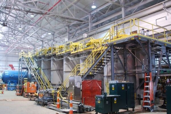 Interior of an industrial facility with metal platforms, stairs, equipment, and safety railings.
