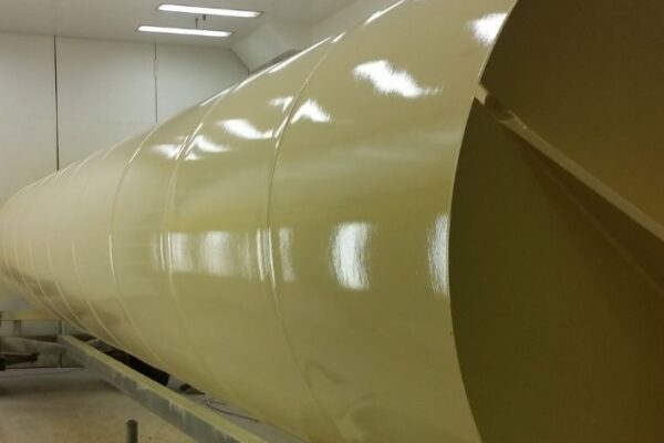 Large, glossy, cream-colored cylindrical industrial tank inside a well-lit facility, viewed from a low angle.