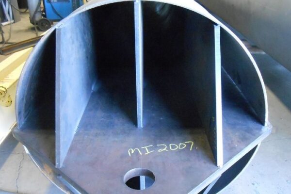 Interior view of a large metal cylinder with welded vertical fins and MI 2007 written in yellow on the base.