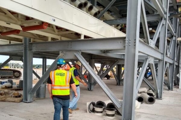 Workers in safety gear inspect a large steel industrial structure at a construction site.