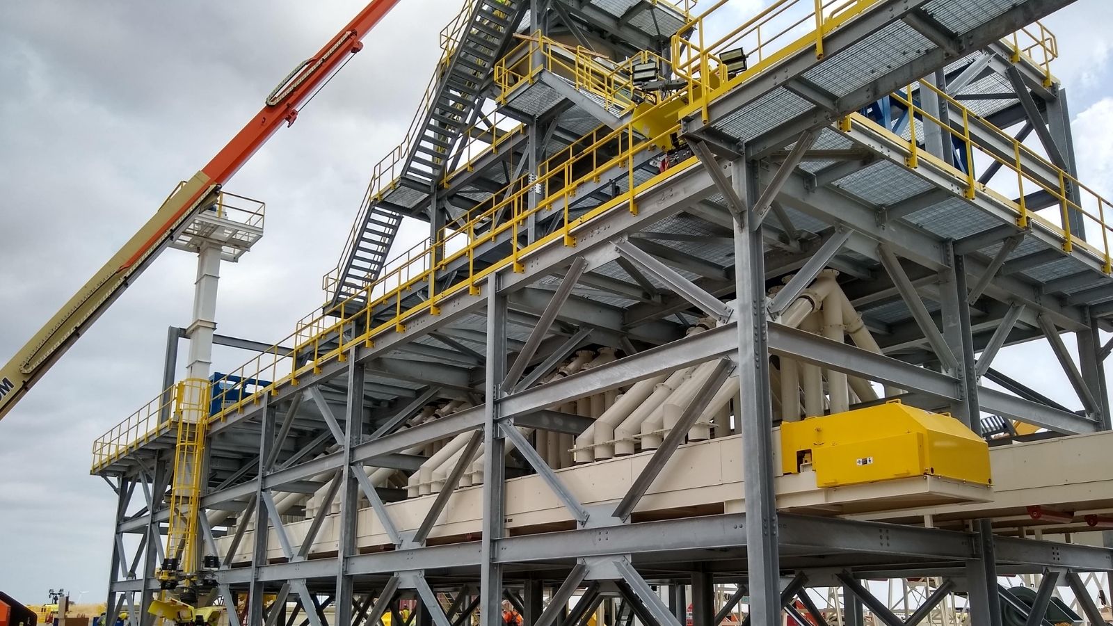 Large industrial steel structure with yellow railings, stairs, and machinery under a cloudy sky.