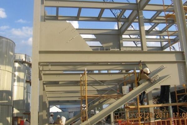 Workers in hard hats assemble a steel building frame using scaffolding under a partly cloudy sky.