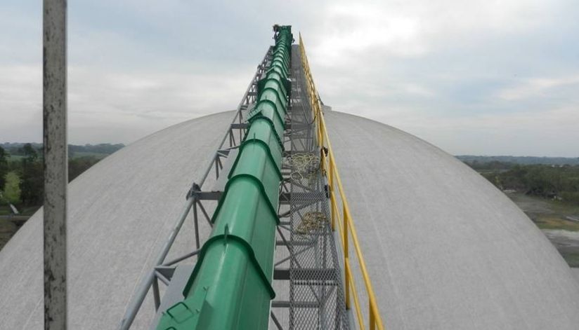 mid-city-steel-la-union-sugar-special-project-gallery-1 Green conveyor belt structure extends up and over a large, dome-shaped industrial building under a cloudy sky.