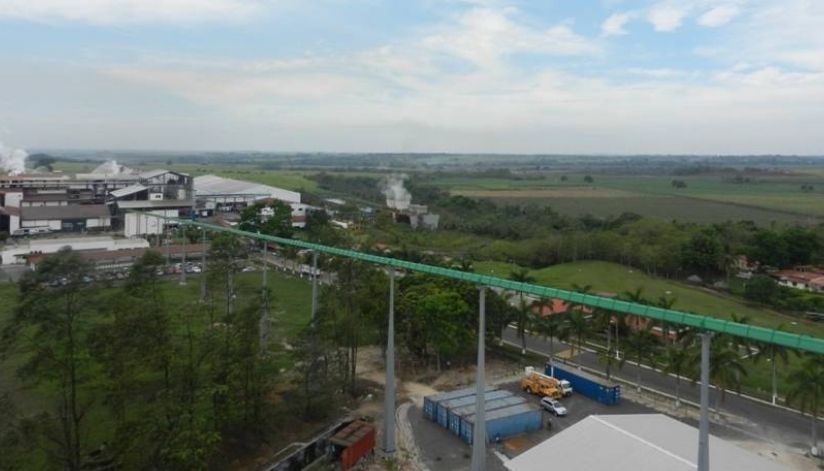 mid-city-steel-la-union-sugar-special-project-gallery-4 Aerial view of an industrial facility with smoke, surrounded by fields, trees, and a long elevated conveyor belt.