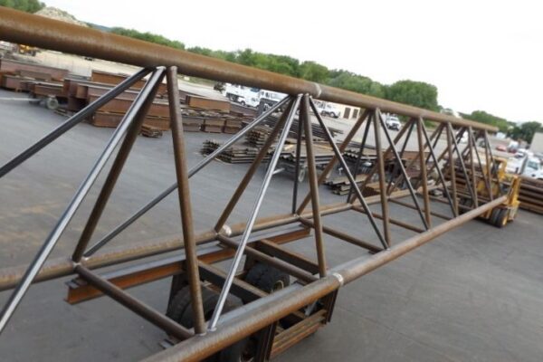 mid-city-steel-mid-city-steel-milwaukee-intermodal-station-special-project-gallery-11 A large metal truss structure on a trailer in an industrial yard with stacks of steel beams in the background.