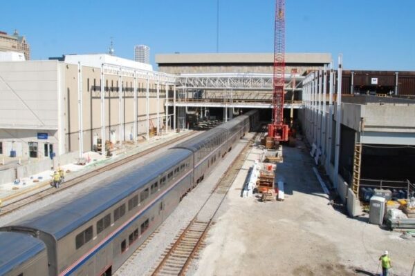 mid-city-steel-mid-city-steel-milwaukee-intermodal-station-special-project-gallery-12 A passenger train departs a station under construction, with workers and equipment visible near the tracks.