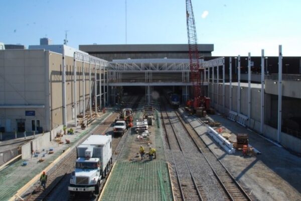 mid-city-steel-mid-city-steel-milwaukee-intermodal-station-special-project-gallery-13 Construction workers and vehicles working on train tracks next to a large building and crane under a clear sky.