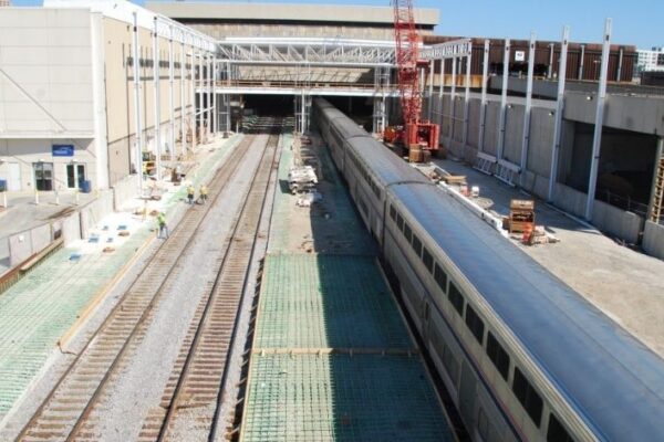 mid-city-steel-mid-city-steel-milwaukee-intermodal-station-special-project-gallery-16 A passenger train is stopped at a station under construction, with workers and building materials nearby.