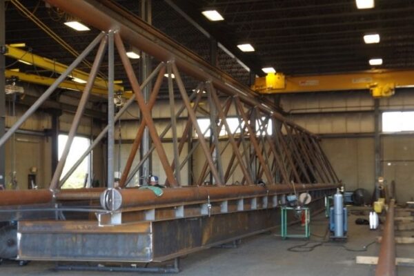 mid-city-steel-mid-city-steel-milwaukee-intermodal-station-special-project-gallery-6 Large steel truss structure being assembled inside an industrial workshop with cranes and equipment visible.