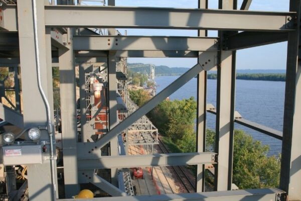 mid-city-steel-pattison-frac-sand-plant-industrial-project-gallery-1 Steel bridge structure above a river, with trees, railroad tracks, and blue sky in the background.