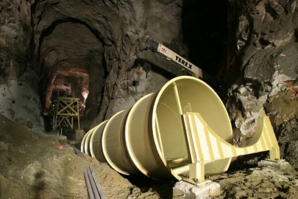 mid-city-steel-pattison-frac-sand-plant-industrial-project-gallery-4 Large metal turbine pipe being installed in an underground cavern, with construction equipment and rocky walls visible.