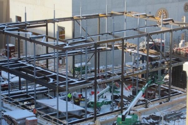 Steel framework of a building under construction with workers and equipment in a snowy urban environment.
