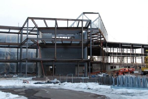 mid-city-steel-uw-superior-swenson-hall-institutional-project-gallery-2 Steel framework of a large building under construction, with snow on the ground and construction equipment nearby.