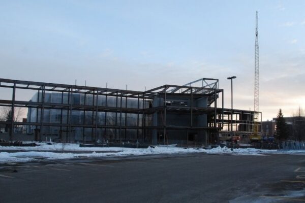 mid-city-steel-uw-superior-swenson-hall-institutional-project-gallery-3 A steel-framed building under construction, surrounded by snow, with a crane in the background at dusk.