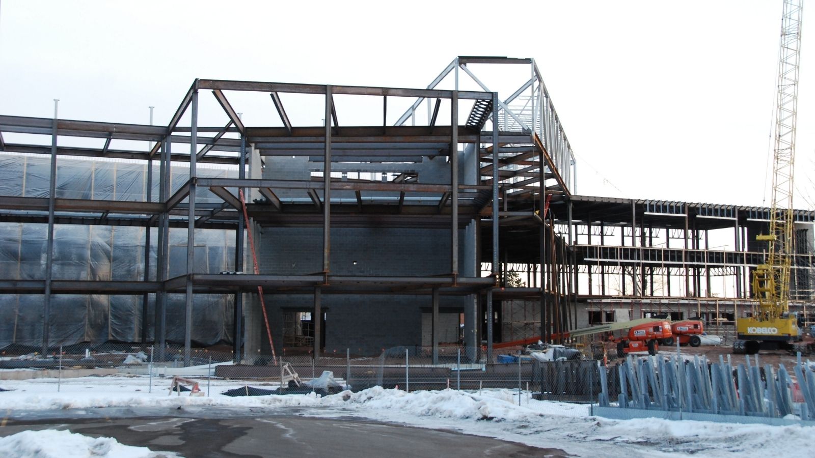 A steel-framed building under construction with snow on the ground and construction equipment nearby.