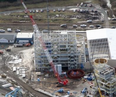 Aerial view of a Mid-City Steel structural steel construction project with multi-story steel framing, cranes, staged materials, and active jobsite operations.