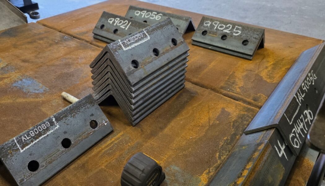 Stacked steel pieces marked with identification numbers on a fabrication table and ready for quality control testing.