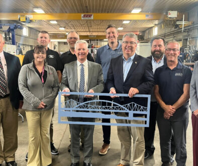 Senator Brad Pfaff, Wisconsin Economic Development Corporation and La Crosse Area Chamber of Commerce representatives, and local business leaders gather inside Mid-City Steel for a roundtable discussion, with a metal bridge cutout displayed in front.